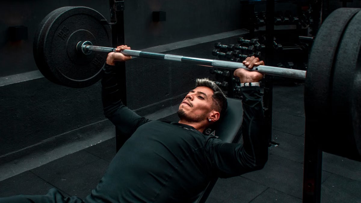 Man performing bench press with heavy barbell in a gym setting, focusing on strength training.